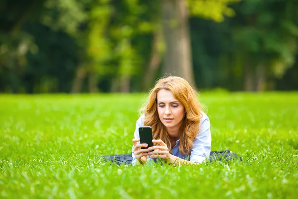 Blonde woman speaking at cellphone in green grass — Stock Photo, Image