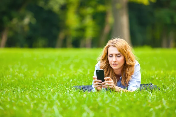 Blonde woman speaking at cellphone in green grass — Stock Photo, Image