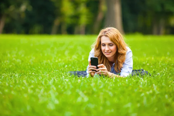 Блондинка говорит по мобильному в зеленой траве — стоковое фото