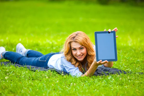 Blonďatá žena leží v zelené trávě s tablet v rukou — Stock fotografie