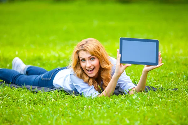 Mujer rubia acostada en hierba verde con una tableta en las manos — Foto de Stock