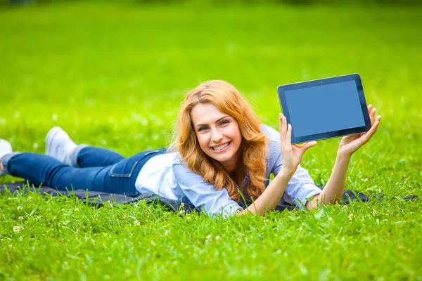 Femme blonde couchée dans l'herbe verte avec une tablette dans les mains — Photo