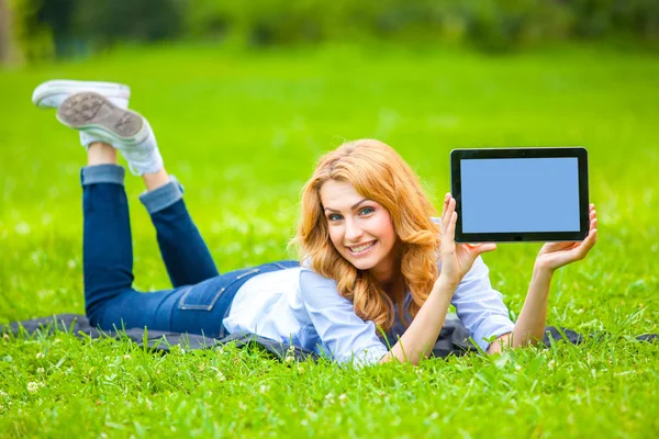 Femme blonde couchée dans l'herbe verte avec une tablette dans les mains — Photo