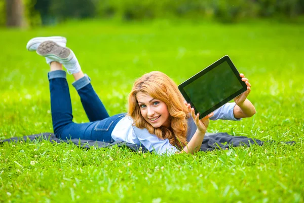 Femme blonde couchée dans l'herbe verte avec une tablette dans les mains — Photo