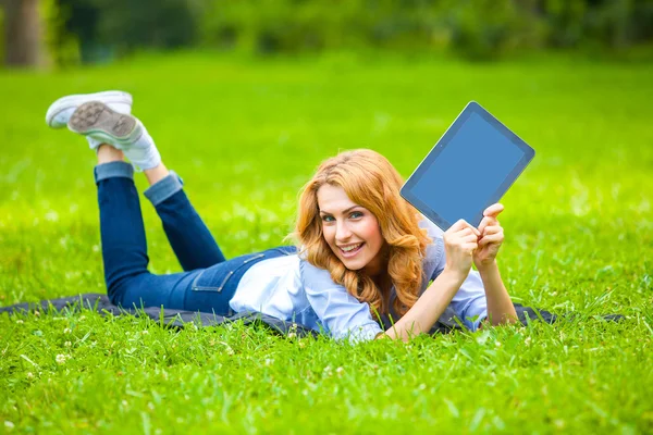 Mujer rubia acostada en hierba verde con una tableta en las manos — Foto de Stock