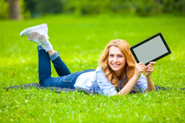 Sarışın kadın ile bir tablet ellerinde yeşil çim yalan — Stok fotoğraf