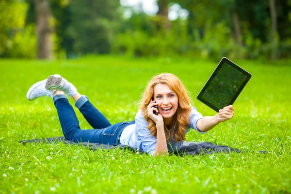 Sarışın kadın ile bir tablet ellerinde yeşil çim yalan — Stok fotoğraf
