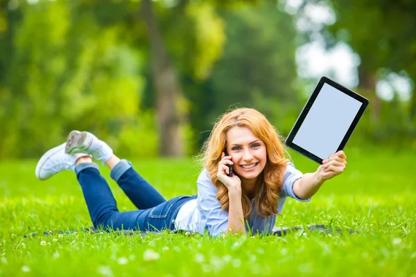 Sarışın kadın ile bir tablet ellerinde yeşil çim yalan — Stok fotoğraf