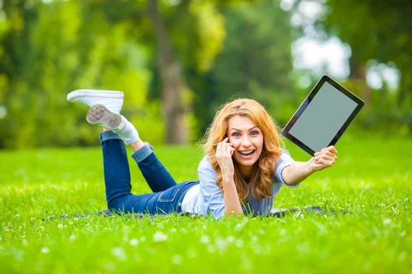 Sarışın kadın ile bir tablet ellerinde yeşil çim yalan — Stok fotoğraf