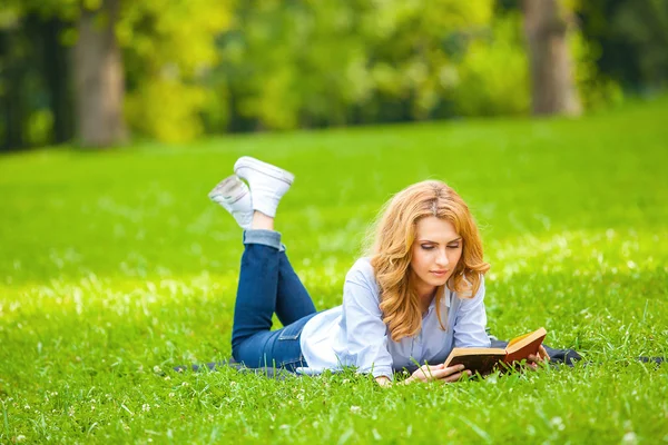 Kvinna ligga i gräset och läsa en bok — Stockfoto
