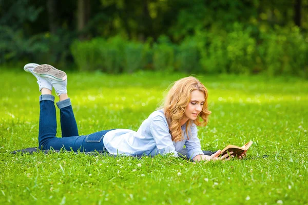Женщина лежит в траве и читает книгу — стоковое фото