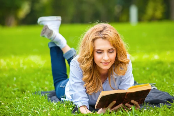 Frau liegt im Gras und liest ein Buch — Stockfoto