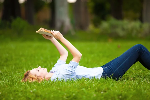 Женщина лежит в траве и читает книгу — стоковое фото