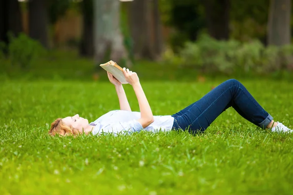 Kvinne som ligger i gress og leser en bok – stockfoto