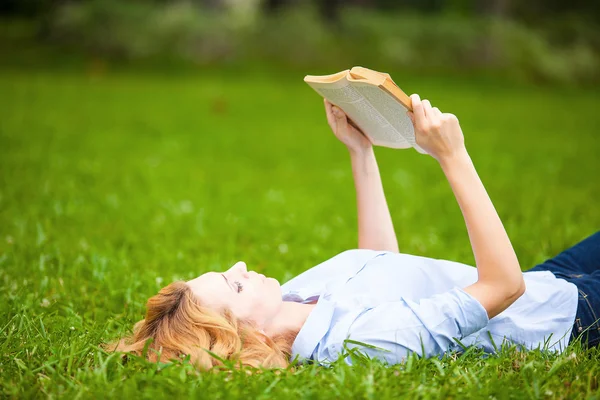 Frau liegt im Gras und liest ein Buch — Stockfoto