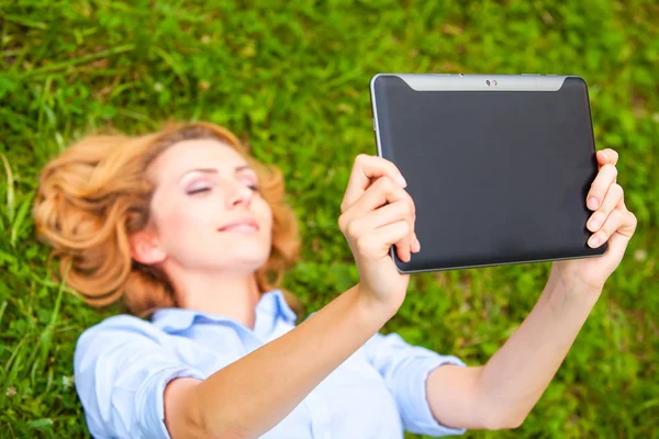 Красивая молодая блондинка лежит в траве с помощью планшета — стоковое фото