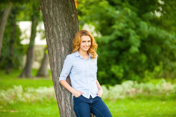 Beautiful young woman standing next to a tree — Stock Photo, Image