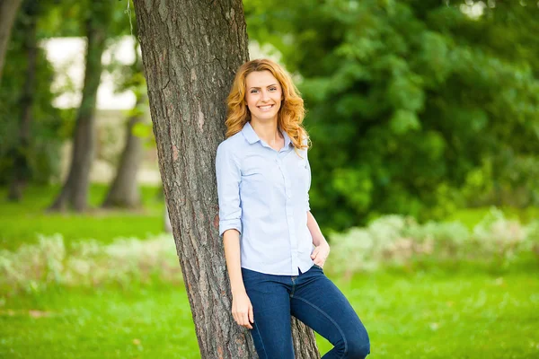 Beautiful young woman standing next to a tree — Stock Photo, Image