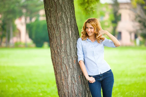 Schöne junge Frau steht neben einem Baum — Stockfoto