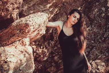 Girl in a black dress posing on a background of sand rocks