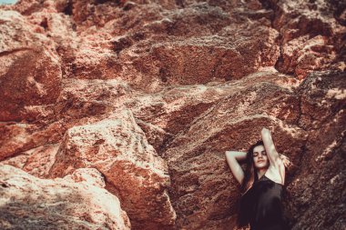 Girl in a black dress posing on a background of sand rocks