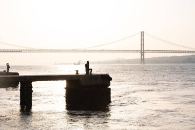 Lizbon 'da gün batımında nehrin önünde bir balıkçının silueti. Portekiz