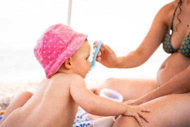 Bikinili bir annenin şemsiyenin altında bir bebeği beslerken çekilmiş fotoğrafı.