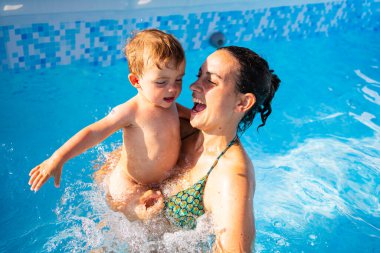 Mutlu bir annenin yazın havuzda oynarken kucağına aldığı bebek görüntüsü.