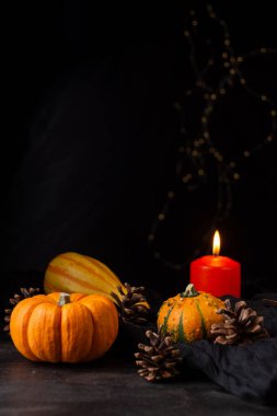 Cadılar bayramı ve yanan turuncu mum için balkabakları yakın plan, seçici odak, koyu ahşap masa, siyah arkaplan ve ışıklar, dikey olarak, kopyalama alanı ile