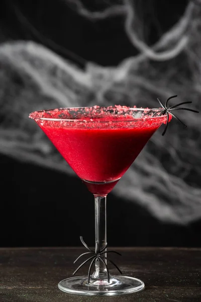 Kırmızı cadılar bayramı kokteyli ile yakın plan, ahşap masa, örümcek ağlı siyah arkaplan, dikey