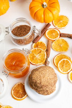 Beyaz masadaki, üzerinde portakal dilimleri, tarçın, balkabağı ve reçel kavanozu olan kurabiyelerin hava manzarası.