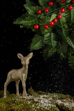 Kar yosunu üzerinde altın Noel geyiği manzarası, yeşil yapraklı siyah arka plan ve kutsal, dikey