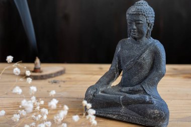 Çiçekler ve tütsü ile koyu renkli Buda figürüne yakın plan, seçici odak, siyah arkaplan, yatay