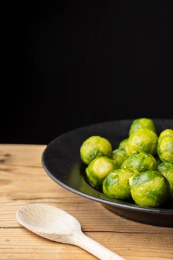 Yeşil lahanalar siyah plaka üzerinde ahşap masa üzerinde ahşap kaşık, seçici odak, siyah arkaplan, dikey
