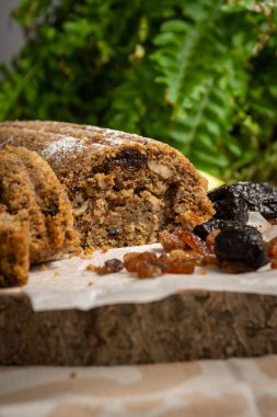Dilimlenmiş kabak keki, kuru üzüm ve erikli, arka planda yeşil yapraklı, seçici odaklı, tahta tabanlı, dikey