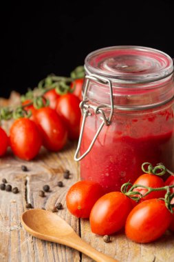 Ev yapımı ketçap kavanozu kaşık, biber ve kiraz domatesli ahşap masa üzerine yakın plan, seçici odak, siyah arka plan, dikey