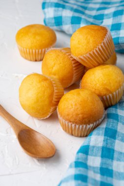 Beyaz ahşap masa üzerinde ev yapımı küçük keklerin üst görüntüsü, mavi kareli kumaş ve tahta kaşık, seçici odak, dikey