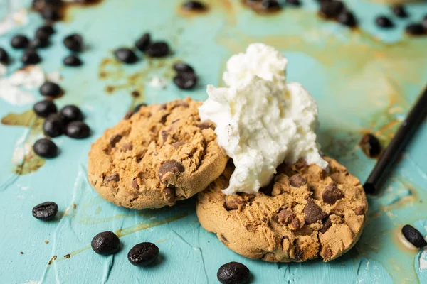 Top view of two cookies with cream on blue table with spilled coffee and grains, horizontal