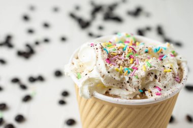 Kremalı kahve ve renkli malzemeli karton fincanın makro üst görüntüsü, kahve çekirdekli beyaz masa, seçici odaklı, yatay