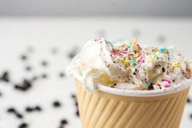 Makro, kahve fincanını kremalı ve renkli malzemelerle kaplıyor, kahve çekirdekli beyaz bir masa üzerinde, seçici odaklı, yatay, kopyalama alanı olan