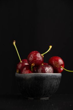 Siyah kasede su damlaları olan kirazların yakın plan çekimi, seçici odak, siyah arkaplan, dikey, kopyalama alanı ile