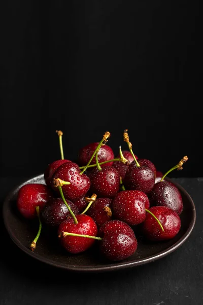 Aerial view of wet cherries on black plate, black background, vertical, with copy space