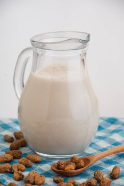 Top view of glass pitcher with horchata and tiger nuts on blue cloth, selective focus, white background, vertical