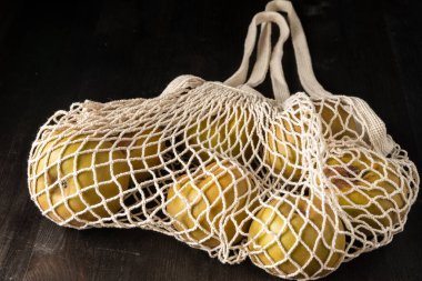 Close-up of white organic net bag with pippin apples, on dark wooden table, black background, horizontal