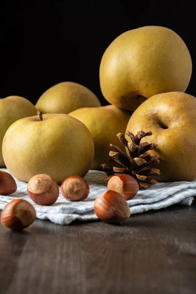 Close-up of pippin apples on blue cloth with hazelnuts, on wooden table, black background, vertical, with copy space