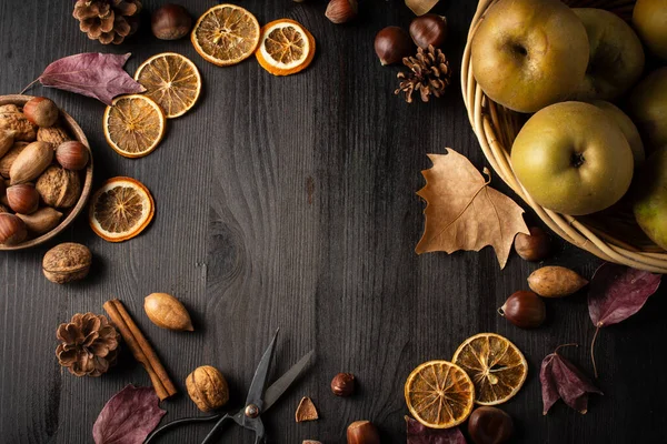 Aerial view in a circle of apples, nuts, oranges and autumn leaves, on a dark wooden background, horizontal, with copy space