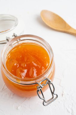 Tahta kaşıkla beyaz masada balkabağı reçeli ile açık cam kavanozun hava görüntüsü, seçici odak, beyaz zemin, dikey, kopyalama alanı ile