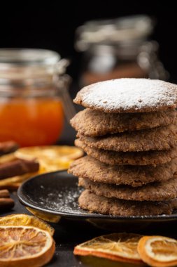 Tereyağlı kurabiyelerin yakın plan portakal dilimleri, tarçın ve kavanozlar ile koyu masa üzerinde, seçici odak, dikey