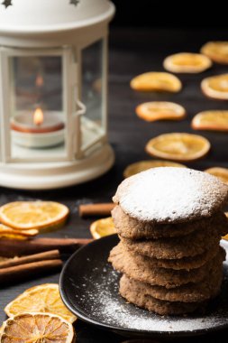 Tereyağlı kurabiyelerin üst görüntüsü koyu renkli masa üzerinde şeker ile portakal dilimleri, tarçın çubukları ve yanan mum ile beyaz fener, seçici odak, dikey