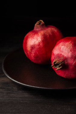 Siyah plakalı iki nar, siyah ahşap masa, siyah arkaplan, dikey, kopyalama alanı olan.